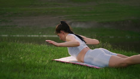 Lying-on-the-mat-the-woman-lifts-the-body-above-the-ground-and-spreads-her-arms-to-the-sides-doing-exercises-for-the-back-muscles